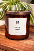 A brown glass candle with a label that reads "Citrus Wood" and "Citrus cedar creme wax hand poured in theUSA".