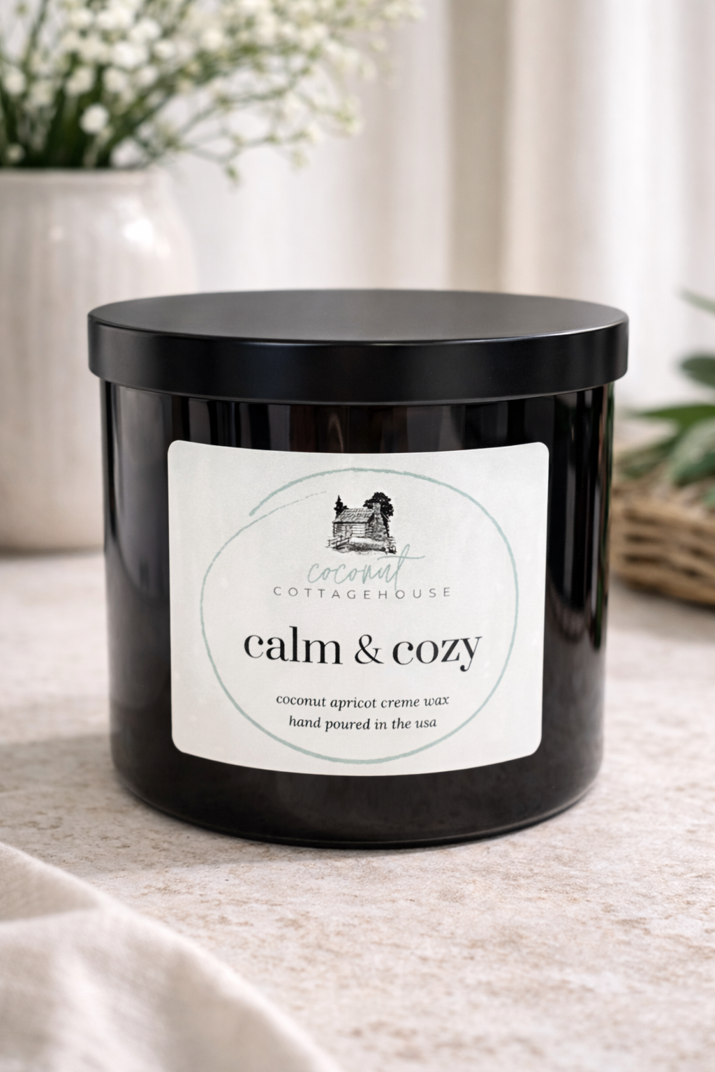 A black candle labeled "Cocoon Cottage" with a label that reads "calm & cozy" and "hand poured in the usa".