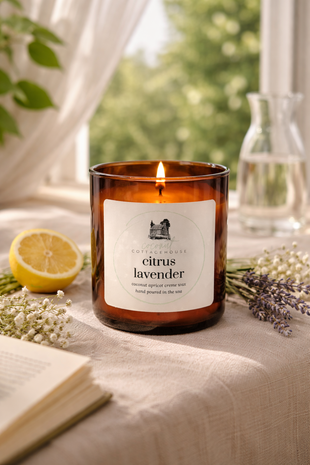 A brown glass candle labeled "Citrus Lavender" sits on a table, surrounded by a lemon slice, a vase of flowers, and a book.