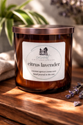 A brown glass candle labeled "Cocoon Cottage" sits on a wooden surface, surrounded by a few purple flowers.