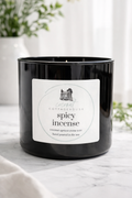 A black candle in a glass container with a label that reads "Coconut Cottage Spicy Incense".