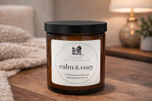 A brown glass candle jar with a label that reads "calm & cozy" and "coconut apricot crème wax hand poured in theUSA".