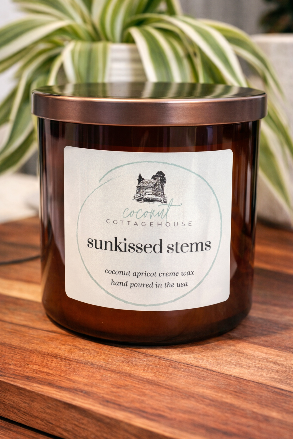 A brown glass candle with a label that reads "sunkissed stems" and "coconut apricot crème wax hand poured in the usa".